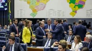 Imagem de assembleia legislativa com representantes estaduais debatendo sobre reforma tributária 2026, mapas do Brasil ao fundo